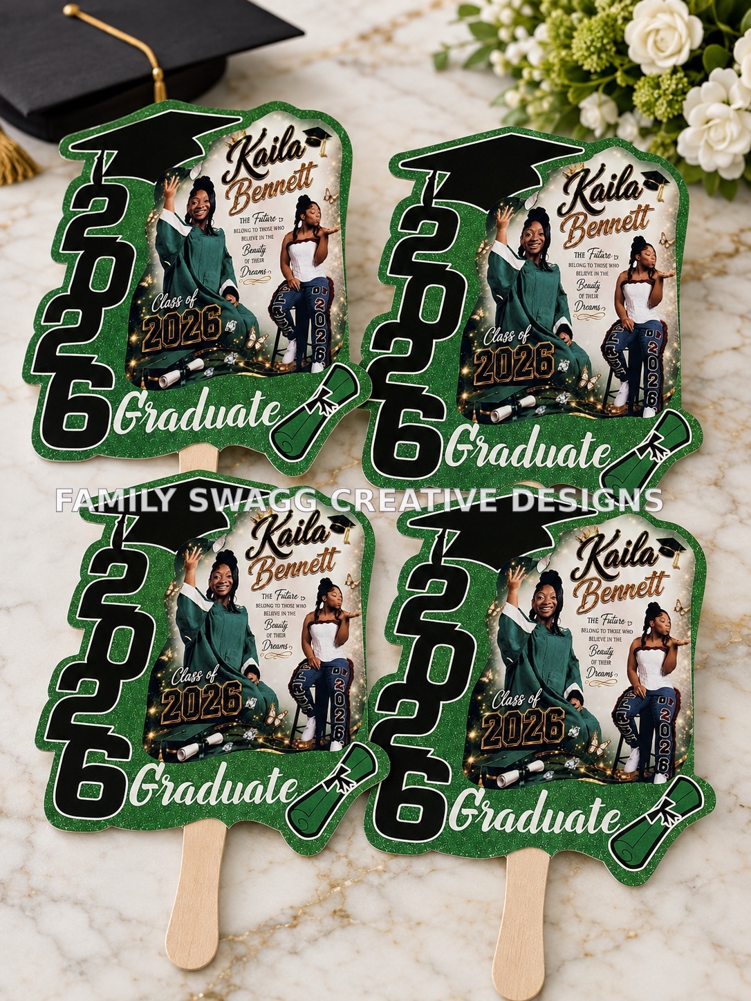 Four green and gold personalized Kaila Bennett Class of 2026 graduation fans displayed on an elegant marble surface